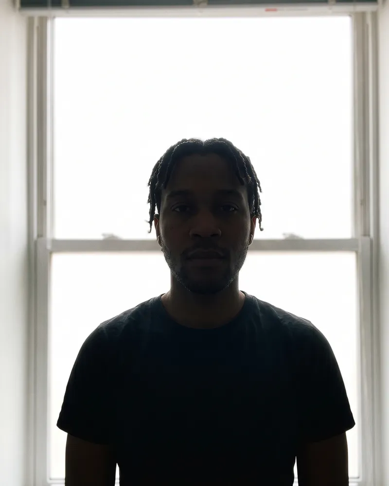 The same man standing in front of a bright window so his face is lost in shadow.